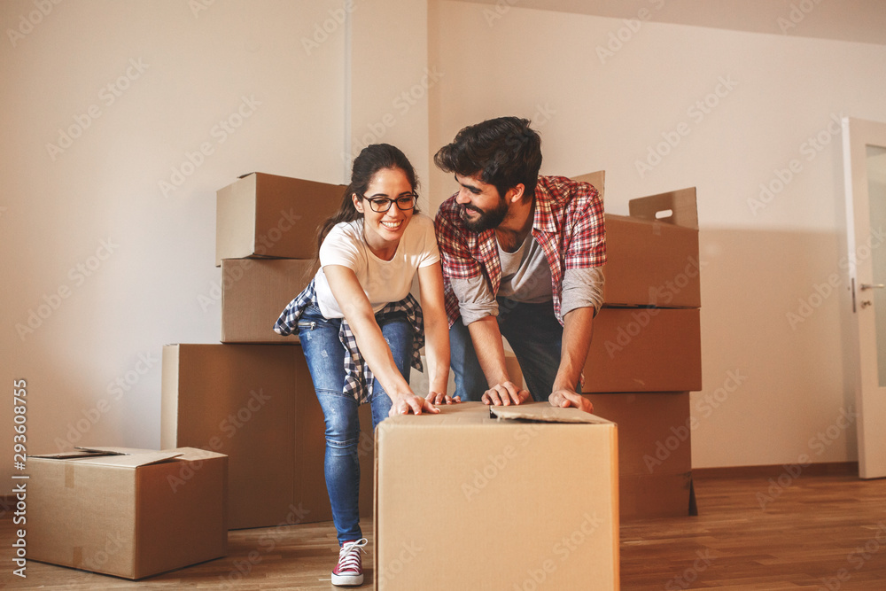 Young couple pushing big cardboard full of home essentials into a new home.Moving house. Young couple pushing big cardboard full of home essentials into a new home.Moving house.