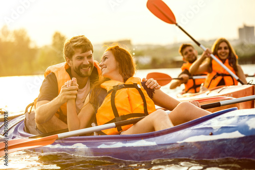 Happy young caucasian group of friends kayaking on river with sunset in the backgrounds. Having fun in leisure activity. Happy male and female model laughting on the kayak. Sport, relations concept.