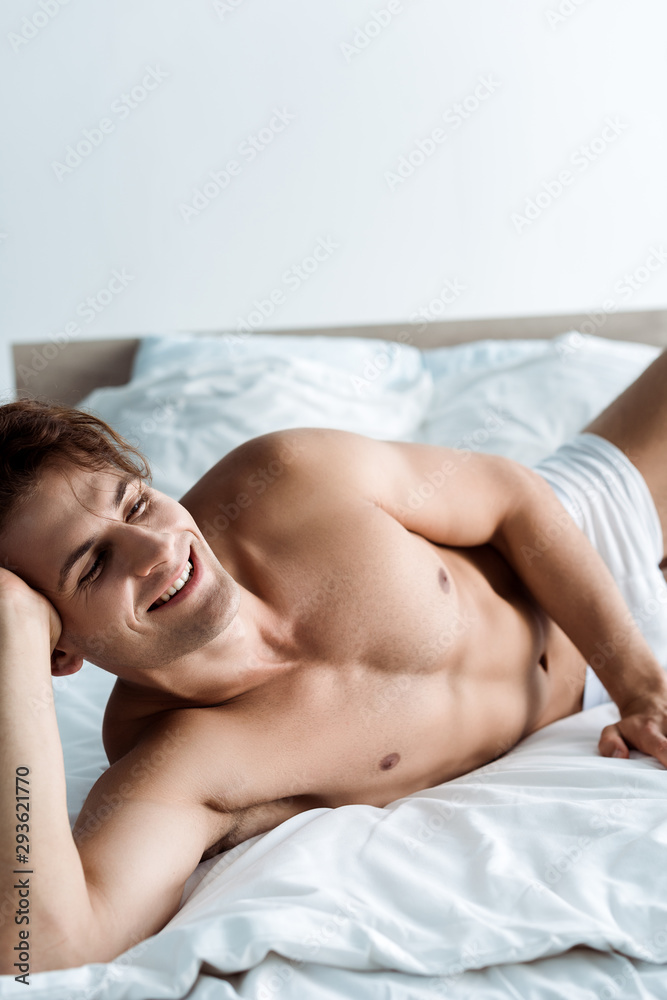 cheerful and sexy man smiling while lying on bed cheerful and sexy man smiling while lying on bed