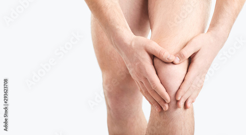 A man in underwear holds his knee with a hand on a gray background.
