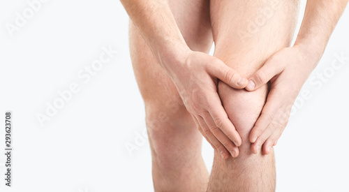 Canvas Print A man in underwear holds his knee with a hand on a gray background