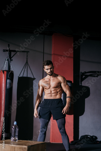 Bodybuilding man portrait standing in front of the camera and posing in a gym class with black background