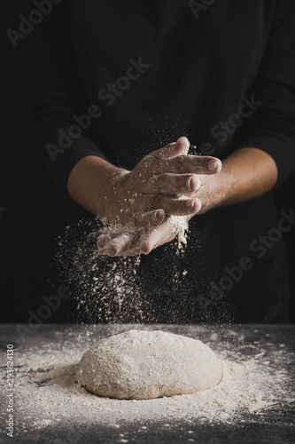 Front view baker spreading flour on dough composition