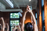 Diverse group of people in yoga class. A young woman is viewed close up and from behind as she stretched her arms towards the ceiling. Spiritual exercises during 108 sun salutes.