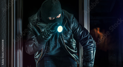 Masked burglar with torch and crowbar breaking and entering into a house - shot with dramatic motion