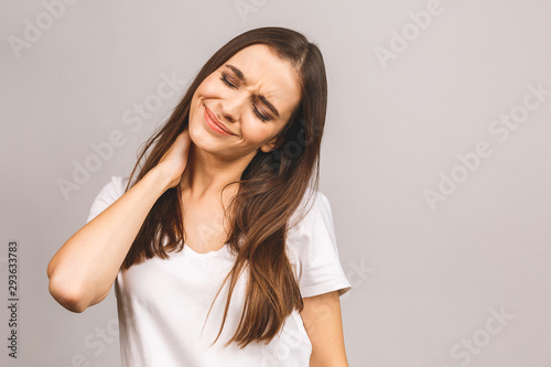 Tired young woman having pain in the neck isolated over grey background.
