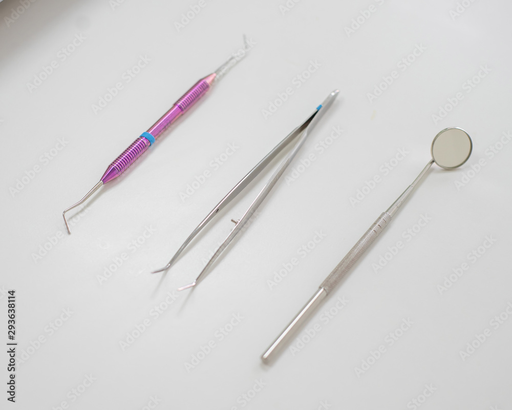 Dentist table with tools on a white background top view. A mirror, tweezers and a probe are on the doctors table. Oral hygiene, caries prevention, examination. Dentist table with tools on a white background top view. A mirror, tweezers and a probe are on the doctors table. Oral hygiene, caries prevention, examination.
