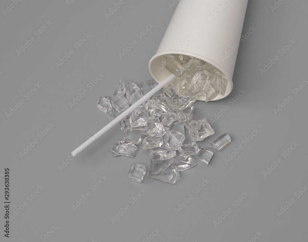 Close up of a paper glass of water with ice cubes spilled on grey background,top view