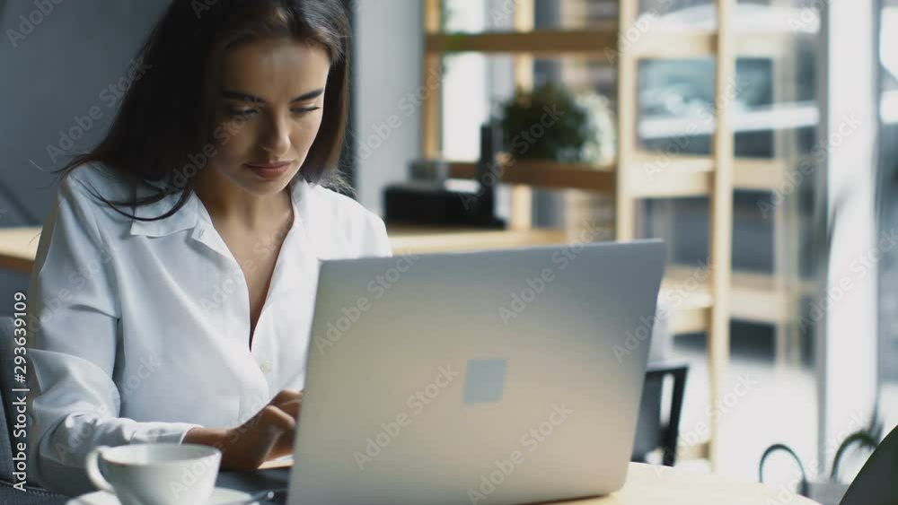happy freelance woman working remotely from her computer in modern cafe