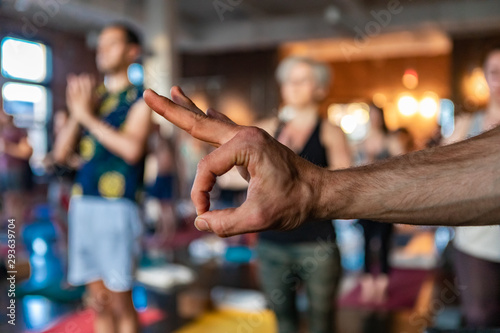 Diverse group of people in yoga class. A motivational gym instructor is seen giving the ok hand gesture inside a gym during a yogic lesson as people are seen in standing pose in the background.