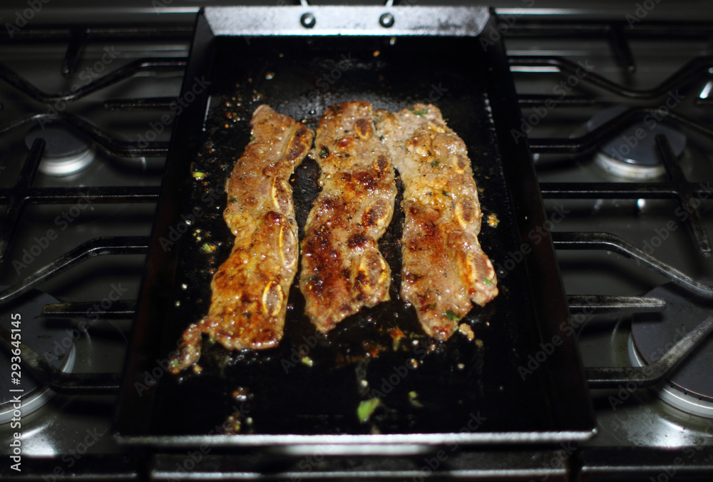 Korean style BBQ short ribs, known as Kalbi, on a carbon steel griddle in a home kitchen. Korean style BBQ short ribs, known as Kalbi, on a carbon steel griddle in a home kitchen.