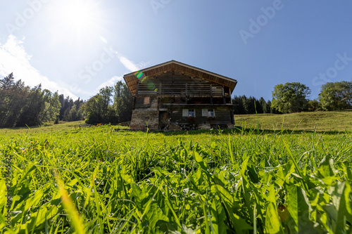 Low and wide angle on a chalet in the french alps with a field of grass in the foreground and the sun shining in the sky