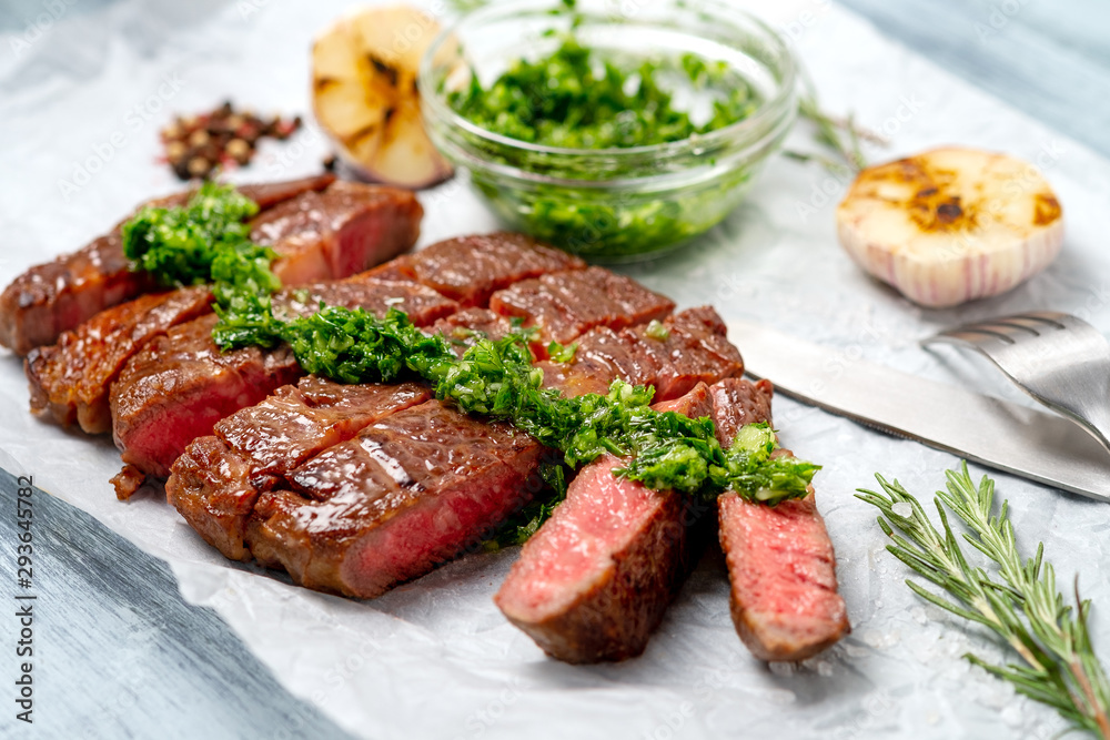 Sliced rib eye beef steak with chimichurri sauce and spices on white paper. Striploin cooked on the grill, top view Sliced rib eye beef steak with chimichurri sauce and spices on white paper. Striploin cooked on the grill, top view