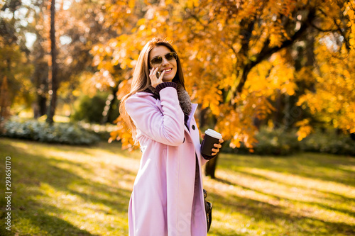 Beautiful woman using phone and drink coffee in autumn park