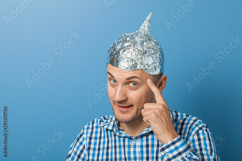 Man with smiles and shows a finger at a hat with aluminum foil. Protects from reading think