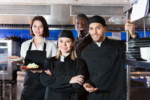 Woman waiter with command of cooks are posing together on kitchen in restaurant.