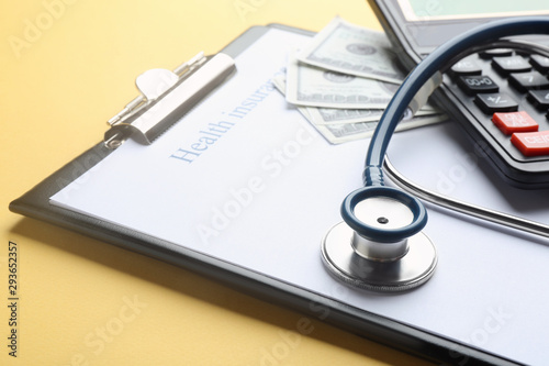 Clipboard with with medical insurance form  money  calculator and stethoscope on yellow background  closeup