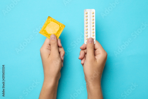 Woman holding condom and birth control pills on blue background, top view. Safe sex