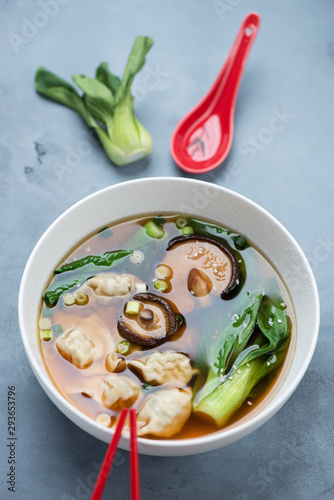 Bowl of wonton soup with pak-choi and shiitake mushrooms, vertical shot over grey concrete background