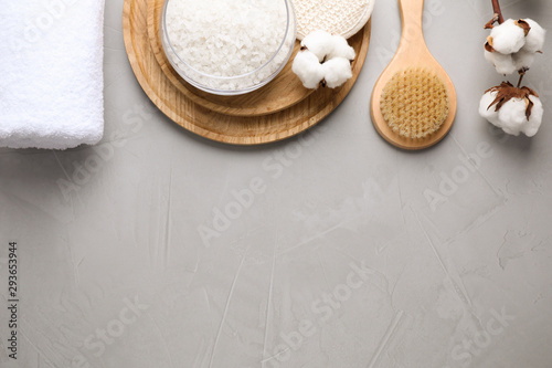 Sea salt and supplies for spa scrubbing procedure on grey stone background, flat lay