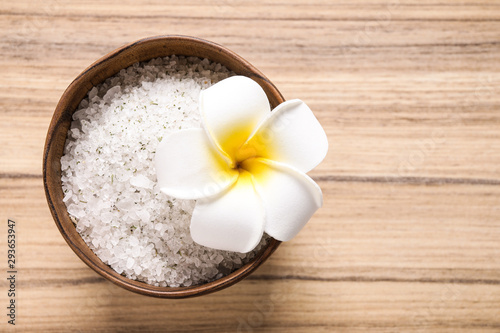 White sea salt for spa scrubbing procedure and flower on wooden background  top view