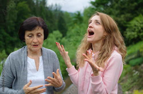 Outdoors portrait of senior mother and adult daughter are communicating outside over landscape of forest and mountains. Two generations, problems between children and parents concept