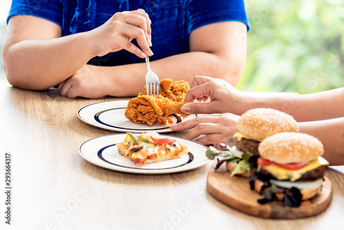 The fat woman sat down to eat together which had fried chicken, pizza and hamburgers, but both fough for the same piece of fried chicken, to food and fat concept.