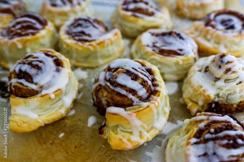 Close-up of homemade puff pastry cinnamon rolls with icing on baking paper
