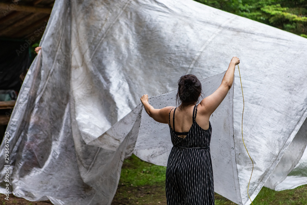 Diverse people enjoy spiritual gathering A young woman is viewed from  behind, erecting a basic tent with a white tarpaulin, during a forest  retreat celebrating nature and diversity. Stock Photo | Adobe