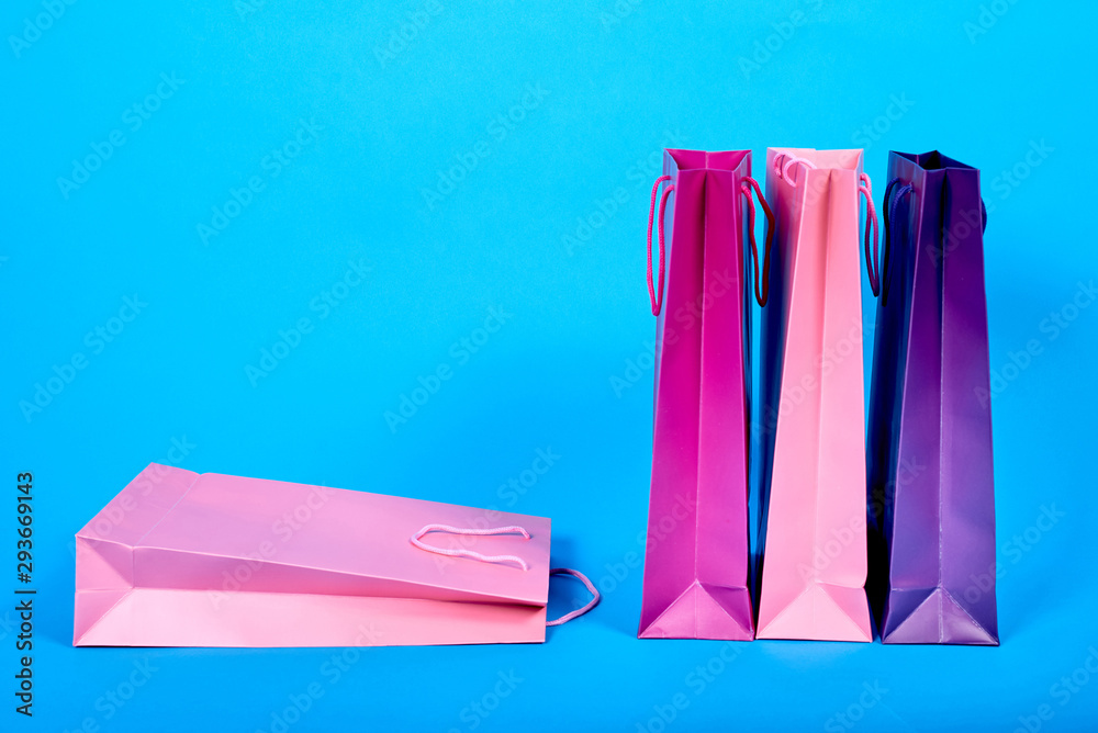 Colorful paper shopping bags isolated on blue background, copy space. Bright gift bags for christmas, birthday presents. Mock up of blank packages with handles