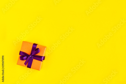 Gift box with ribbon and bow on yellow background and space for text. Top view 