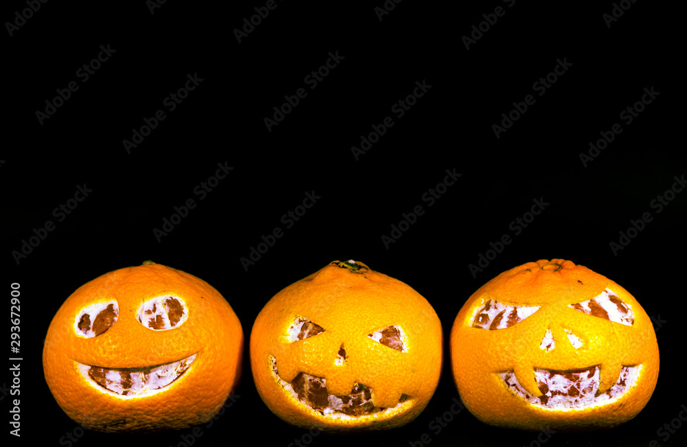 Grapefruit, tangerines and oranges are isolated on a black background in the form of a halloween pumpkin. A scary face is carved on grapefruit, tangerines and oranges. Grapefruit, tangerines and oranges are isolated on a black background in the form of a halloween pumpkin. A scary face is carved on grapefruit, tangerines and oranges.