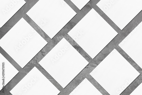 White empty square business card mockups with soft shadows lying diagonally on elegant dark grey concrete background. Flat lay, top view. Open composition.