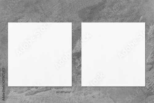 Two empty white square flyer or business card mockups with soft shadows on elegant dark grey concrete background. Flat lay, top view