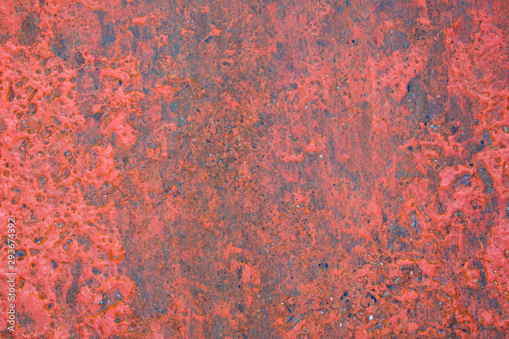 old gray concrete wall with protruding stones and peeling bright red paint. rough surface texture
