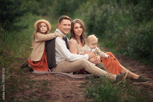 family with two children sitting on the ground in the forest and smiling at the camera