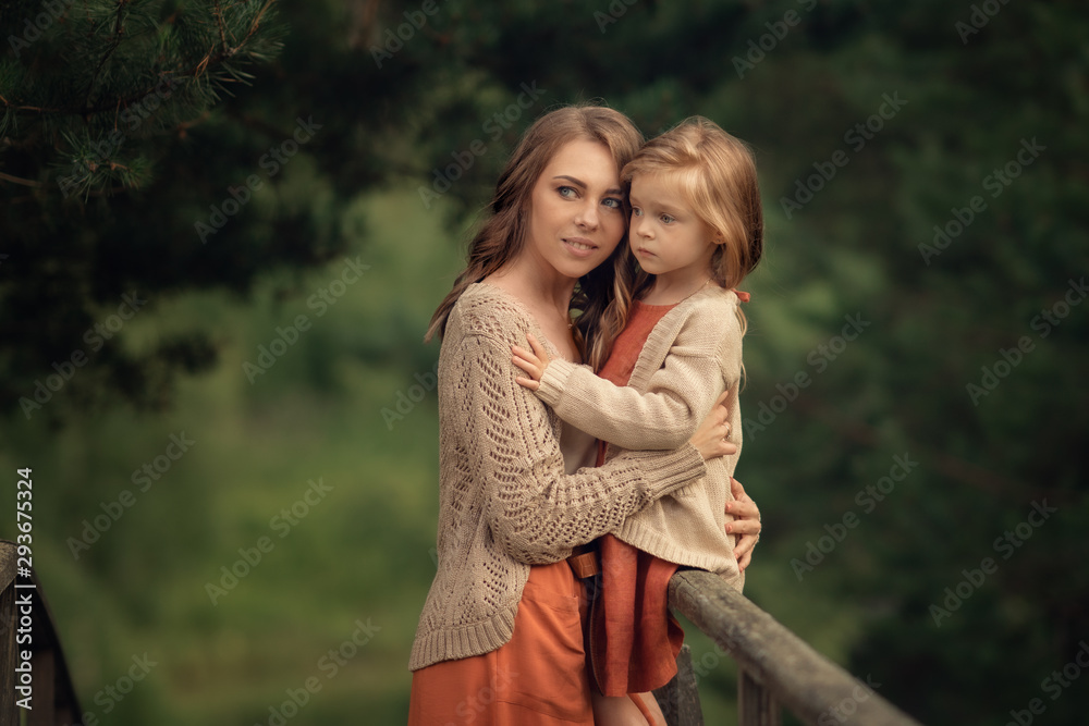 Fototapeta premium young mother hugging her daughter sitting on the wooden railing in the forest