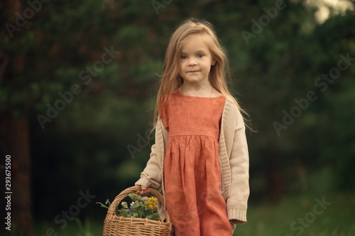 portrait of cute child holding flowers in wicker basket and looking at the camera outdoors