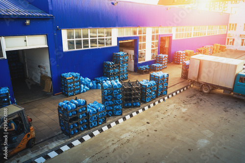 Aerial view of freight warehouse of drinking water plant or factory in sunlight, racks with plastic bottles or gallons ready for loading at trucks © DedMityay