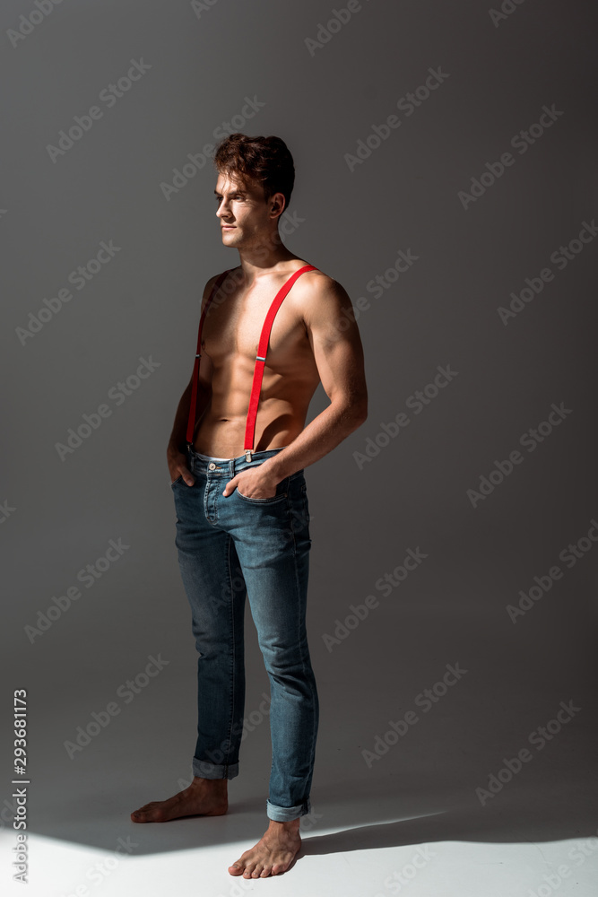 shirtless and handsome man touching red suspenders while standing on grey shirtless and handsome man touching red suspenders while standing on grey