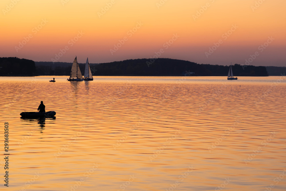 Fishing early in the morning. silhouette of fishermen in a boat on a lake. Sailing boats at sunset on background