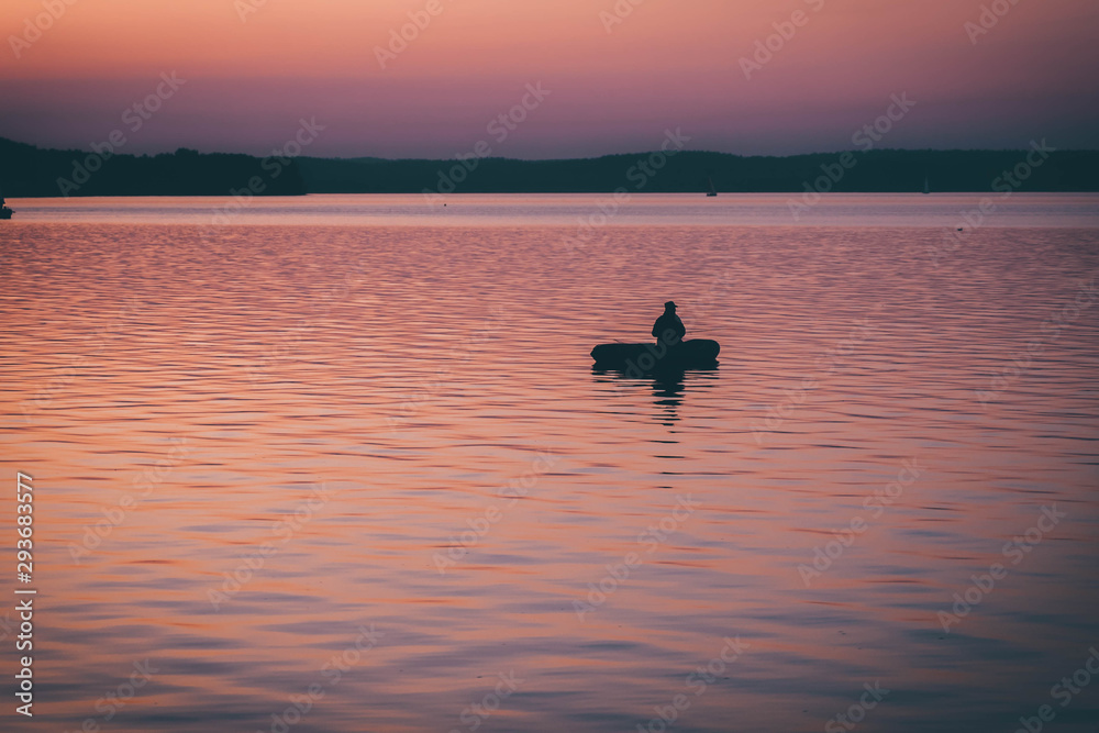silhouette of fishermen alone in a boat swimming on a lake. sunset background.