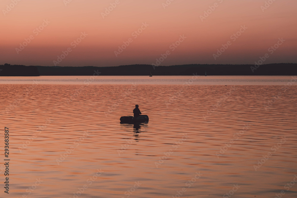 Naklejka premium silhouette of fishermen alone in a boat swimming on a lake. sunset background.