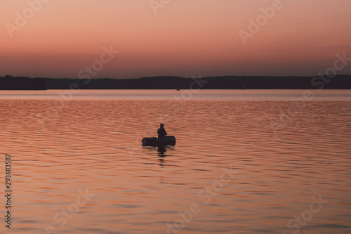 silhouette of fishermen alone in a boat swimming on a lake. sunset background.