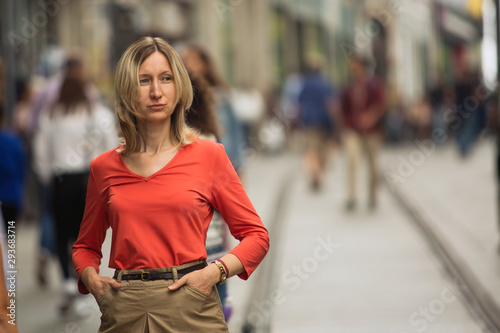 Blond woman in a red blouse standing on the street.