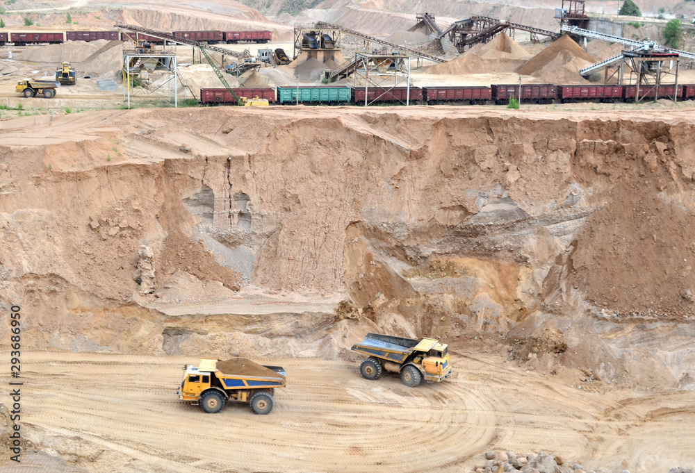 Big yellow dump trucks working in the open-pit. Transporting sand and minerals. Mining quarry for the production of crushed stone, sand and gravel for use in the construction industry - image Big yellow dump trucks working in the open-pit. Transporting sand and minerals. Mining quarry for the production of crushed stone, sand and gravel for use in the construction industry - image