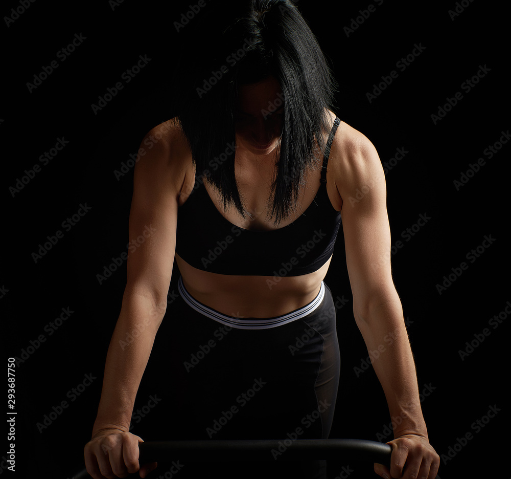 Obraz premium young beautiful athletic girl with muscles in a black bra is wrung out in her arms