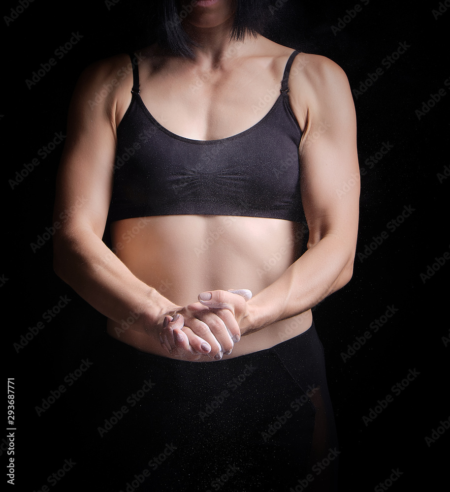 beautiful young girl with a sports figure dressed in a black top claps in her hands with white magnesia