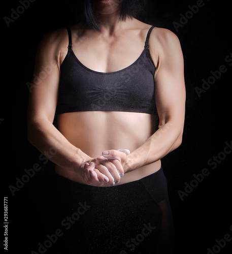 beautiful young girl with a sports figure dressed in a black top claps in her hands with white magnesia