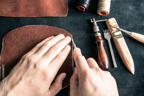 a young tanner on a desktop in a workshop chamfers a piece of brown leather with a special tool